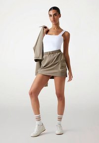 Bēša krāsas sporta šorti ar elastīgu jostasvietu un kabatām, kopā ar piegulošu baltu tanktopu un saskaņotu bēšu krāsas jaku. Baltas sporta kurpes ar svītrainām zeķēm.