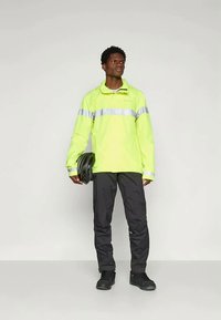 Højtsynlig gul vandtæt jakke med grå reflekterende striber, parret med sorte bukser og sort hjelm. Glat tekstur, praktisk design.