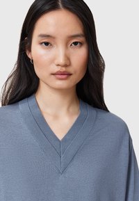 Grijze gebreide top met een V-hals ontwerp, zachte textuur en zichtbare stiksels langs de halslijn, gedragen door een model.