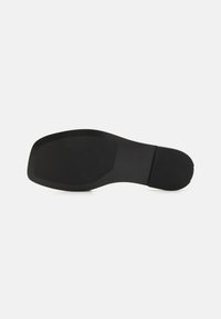 Black rubber shoe sole with a flat, rectangular shape. Textured grip area at the heel and a smooth surface overall. No patterns or accents.