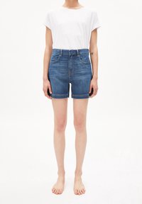 Modré džínové kraťasy s vysokým pasem a ohrnutým lemem, přední a zadní kapsy, v kombinaci s jednobílým tričkem. Měkká textura. Bez vzorů.