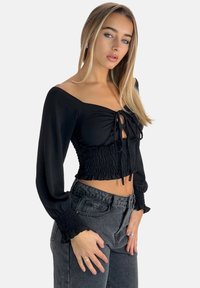Top corto nero arricciato con maniche lunghe e leggermente a sbuffo e un design con fiocco frontale. Presenta un tessuto testurizzato e un orlo corto.