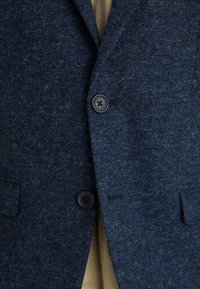 Blazer in lana blu navy con finitura testurizzata, dotato di due bottoni frontali, tasche laterali e un classico colletto a punta.