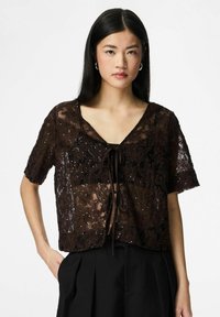 Brun bluse med korte ermer i blonder, med blomsterdesign, V-utringning og knytedetalj foran. Gjennomsiktig tekstur med subtile utsmykninger.