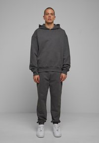 Mørkegrå hættetrøje med en lomme foran og snøre i hætten, parret med matchende grå joggere og hvide sneakers. Glat stoftekstur.