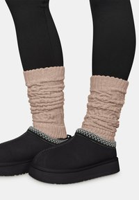 Schwarze Stiefeletten mit strukturierter Oberfläche, verziert mit einem Zickzackstich entlang des Kragens, kombiniert mit gerafften beigen Strick-Stulpen.