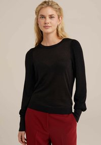 Juodas megztinis su ilgomis rankovėmis ir apvalia iškirpte. Savyje turi subtilų blizgesį ir prigludusį ripsinį apatinį kraštą. Derinamas su raudonomis kelnėmis.