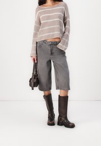 Beige gestreifter Strickpullover, graue weit geschnittene Jeansshorts, braune knielange Lederstiefel und eine kleine dunkle Handtasche.