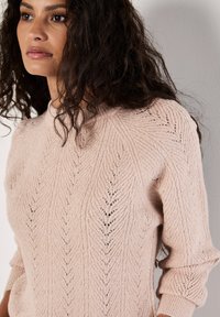 Jasnoróżowy sweter dzianinowy z teksturowanym wzorem liści, z długimi rękawami i wysokim kołnierzem, wykonany z miękkiego, błyszczącego materiału.