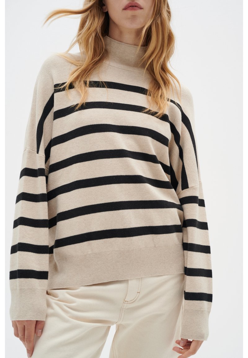 Pull beige à rayures horizontales noires, col montant et manches larges. Texture douce, poignets et ourlet côtelés pour une coupe décontractée.