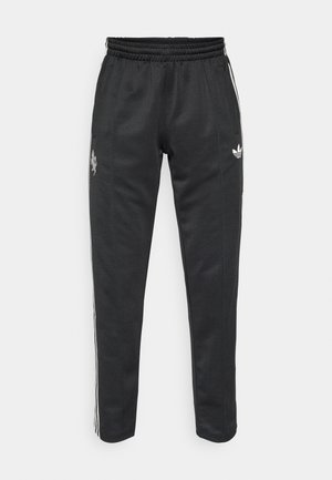 Pantalon de sport noir à coupe ajustée, avec des bandes blanches sur les côtés et un logo brodé à l'avant, fabriqué en tissu lisse et extensible.