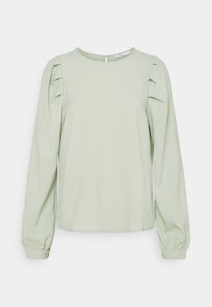 Ljust grön blus med lång ärm och subtil textur, rund halsringning och puffade axlar. Har en knapp på baksidan och rynkade ärmar.