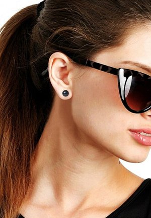 Boucles d'oreilles rondes noires portées dans le lobe de l'oreille, assorties à des lunettes de soleil surdimensionnées noires et écaille de tortue, mettant en avant un design élégant.