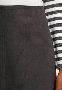 Jupe en daim noire au texture lisse, avec des coutures verticales. Associée à un haut à manches longues blanc et noir à rayures.