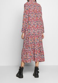 Abito maxi floreale in rosa, con maniche lunghe, colletto e design a strati, decorato con motivi floreali colorati. Abbinato a stivaletti neri alla caviglia.