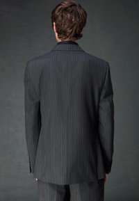 Schwarze Nadelstreifen-Anzugjacke mit Reverskragen, zwei Knöpfen und strukturiertem Stoff. Die Rückansicht zeigt die taillierte Passform und die Ärmelknöpfe.