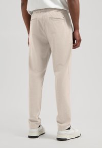 Lyse beige joggebukser med elastisk midjebånd, sidelommer og to baklommer, kombinert med hvite joggesko. Glatt tekstur.