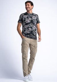Camiseta negra con flores en patrones rosados y verdes, combinada con pantalones cargo beige que tienen múltiples bolsillos y un corte recto, llevados con zapatillas blancas.