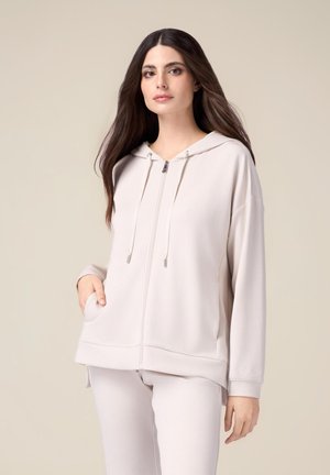 Sudadera con cremallera de color beige claro, con capucha, cordones, bolsillos frontales y puños de canalé, hecha de una tela suave con una textura lisa.