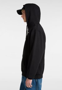 Felpa nera con cappuccio realizzata in misto cotone, con tasca frontale, cordino e logo sul petto. Indossata con jeans in denim blu.