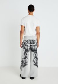 Gray sweatpants with black graphic prints, wide-leg design, and elastic waistband. Paired with a plain white short-sleeve t-shirt.