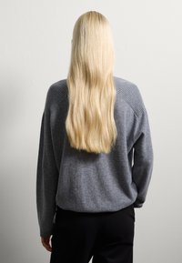 Grijze wollen trui met een comfortabele, losse pasvorm en een textuur met ribbeldetails op de schouders, gecombineerd met strakke zwarte broek.