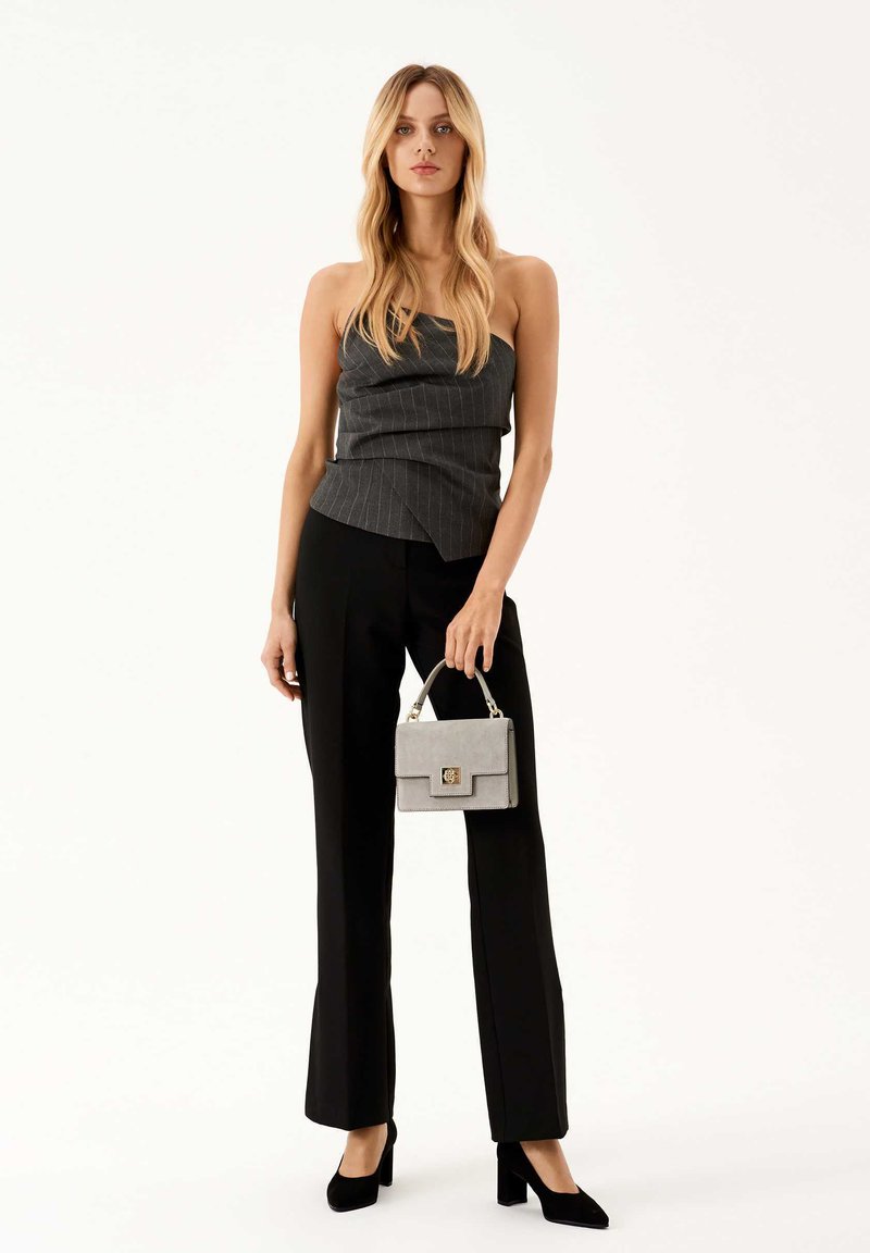 Gray pinstriped peplum top paired with black tailored pants and black block heels. Gray handbag with a clasp detail in hand.
