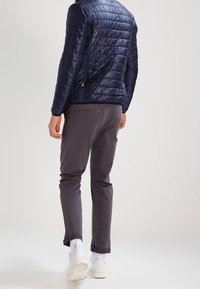 Marinblå quiltad pufferjacka med zip, parat med grå chinos och vita sneakers. Slät textur och lätt design är framträdande egenskaper.