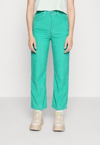 Pantalones de pana verdes con un diseño de pierna recta, que presentan una cintura alta y una textura en la tela, combinados con zapatillas beige.
