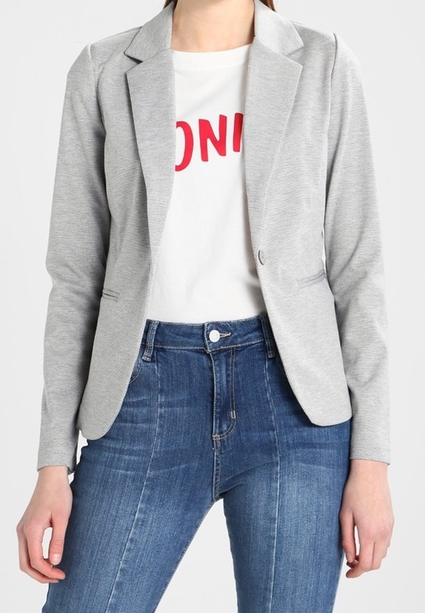 Blazer gris à revers crantés, fermeture par un seul bouton, associé à un T-shirt blanc avec inscription rouge et un jean en denim bleu.