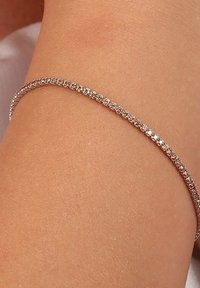 Bracciale in oro rosa con un design delicato e piccole accentuazioni di cristallo lungo tutta la sua lunghezza, curvato delicatamente per adattarsi al polso.