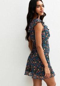 Vestido floral de tela negra con patrones coloridos, mangas con volantes y cintura ajustada, terminando por encima de la rodilla para un look fluido.