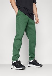 Grønne sweatpants med en blød tekstur, elastisk talje, og sidelommer, parret med sorte træningssko med hvide accenter.