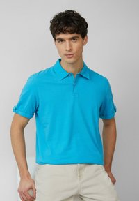 Turquoise poloshirt met een kraag, korte opgerolde mouwen en knoopaccenten. Gemaakt van soepel materiaal, met een ontspannen pasvorm en een effen ontwerp.