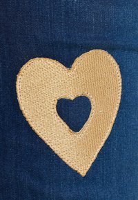 Džínovina s velkou, světle hnědou vyšívanou nášivkou ve tvaru srdce s menším výřezem srdce uprostřed. Hladká textura a detailní šití.