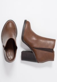 Stivaletti marroni in pelle con finitura testurizzata, dotati di un tacco a blocco spesso e di un pannello elastico laterale per una calzata più facile.