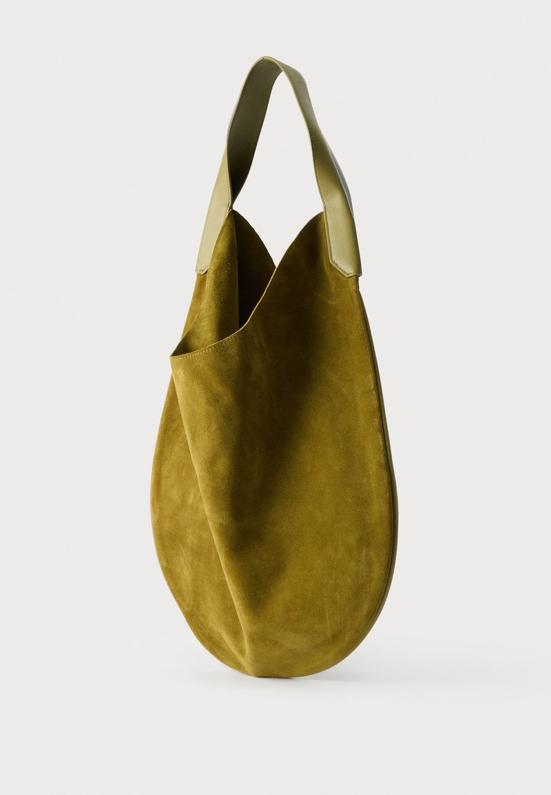 Sac cabas en daim vert olive doux avec une large anse en cuir et une forme souple et arrondie sur un fond uni.