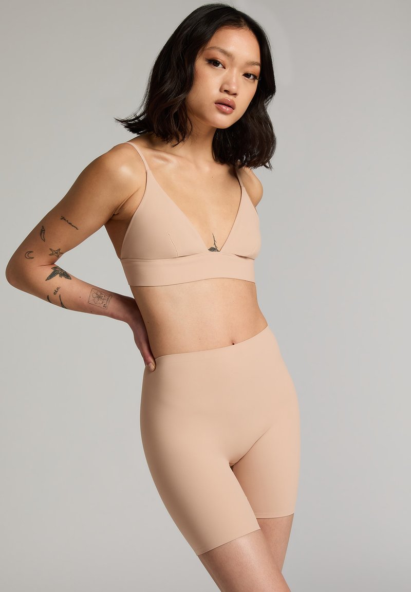 Nude seamless bralette met dunne bandjes en een V-hals ontwerp, vergezeld van bijpassende high-waisted fietsbroekjes, met een gladde textuur.