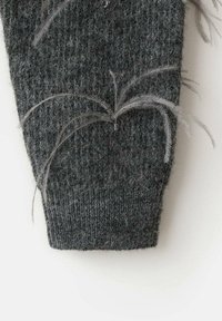 Manche de pull gris tricoté avec un motif texturé ; ornée d'accents gris en plume qui dépassent du tissu.