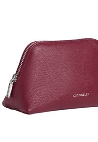Bordowa skórzana torba z teksturowanym wykończeniem, srebrnymi akcesoriami i zakrzywionym zapięciem na zamek. Na przedniej części znajduje się wytłoczone logo marki.