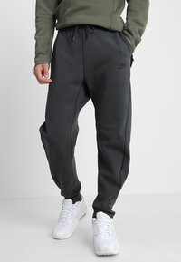 Mörkgrå bomullsbyxor med avsmalnande ben och elastisk midja. Har sidfickor och en subtil logotyp. Kombineras med vita sneakers.