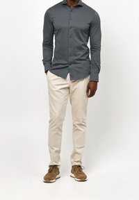 Tmavě šedá dlouhá košile s knoflíky ve slim fit střihu, v kombinaci se světle béžovými kalhotami a hnědými teniskami. Hladký materiál, jednoduchý design.