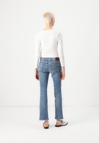 Vaqueros acampanados de color azul claro con cintura de altura media, que cuentan con cinco bolsillos y una etiqueta de cuero marrón en la parte trasera, combinados con una camiseta blanca de canalé.