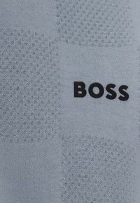 Jasnoniebieska teksturowana tkanina z subtelnym wzorem, na której widnieje nazwa marki "BOSS" w grubych czarnych literach.