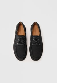 Črne usnjene čevlje z vezalkami in zaobljenim nosom, z vidnim šivanjem in svetlo rjavim notranjim vložkom. Oblikovanje vsebuje minimalne poudarke in gladko teksturo.