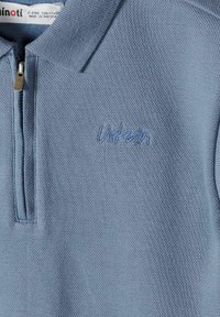 Polo bleu clair texturé avec fermeture éclair, petit texte brodé "urban" sur la poitrine, et étiquette indiquant la taille 5-6 ans.