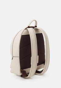 Mały kremowy skórzany plecak z wyściełanym ciemnobrązowym tyłem z siateczki i dopasowanymi regulowanymi paskami na ramiona.