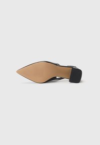 Scarpa nera con punta affusolata, realizzata in materiale lucido, suola beige e tacco grosso accentuato da un pannello nero testurizzato.
