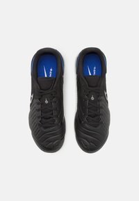 Pár černých sportovních bot s modrými vložkami a bílým logem swoosh, zobrazených shora na bílém pozadí.