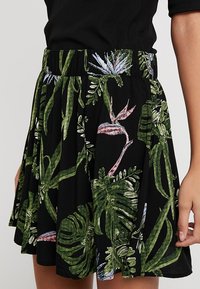 Jupe noire avec une taille froncée arborant un imprimé de plante tropicale en vert, rose et bleu. Tissu lisse avec un design évasé.
